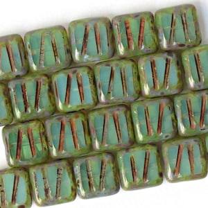 Può includere: Una collezione di perline quadrate in vetro verde con un interno blu chiaro e linee marroni. Le perline hanno una smaltatura verde screziata.