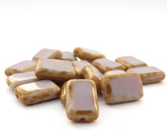 May include: A collection of rectangular beads with a smooth, glossy finish. Each bead features a pale lavender centre framed by a mottled, light brown border. The beads are arranged in a small pile, showcasing their uniform shape and reflective surface.