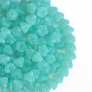 Könnte beinhalten: Ein Haufen türkisblauer Glasperlen in Blütenform. Die Perlen sind durchscheinend und haben einen leichten Schimmer.