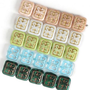 Könnte beinhalten: Eine Sammlung quadratischer Perlen in verschiedenen Farben, darunter Rosa, Weiß, Grün, Blau und Dunkelgrün. Jede Perle hat ein goldfarbenes, verziertes Design in der Mitte. Die Perlen sind in Reihen angeordnet und zeigen ihre dekorativen Muster.