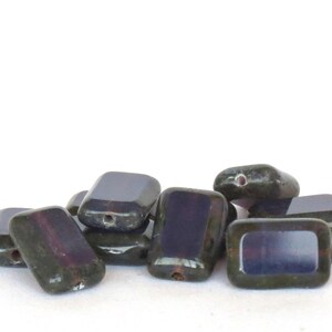 May include: A group of dark green and purple glass beads with a rectangular shape. The beads have a hole in the center for stringing.