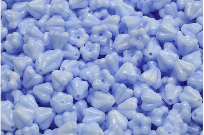 May include: A large pile of light blue glass beads with a flower shape. The beads have a glossy finish and are perfect for jewelry making.
