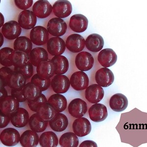 Op de afbeelding: Een stapel donkerrode ronde glazen kralen van 6 mm.