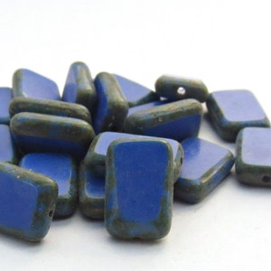 Op de afbeelding: Een stapel blauwe en groene rechthoekige glazen kralen. De kralen hebben een gemarmerde groene glazuur aan de randen en een gladde blauwe glazuur aan de bovenkant.