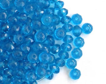 May include: A pile of turquoise blue glass beads with a faceted finish. The beads are round and have a hole in the center.