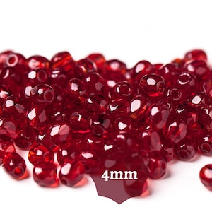 Pode incluir: Uma pilha de contas facetadas, vermelho escuro, cada uma com aproximadamente 4 mm. As contas estão agrupadas, refletindo a luz e criando um efeito brilhante. A imagem está em um fundo branco.