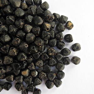 May include: A pile of black, multi-faceted beads with a worn, aged look. The beads have a matte finish with gold or tan highlights, and each has a hole for threading. These beads are suitable for jewellery making.
