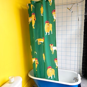 Könnte beinhalten: Eine blaue und weiße Klauenfußbadewanne mit einem grünen Duschvorhang mit einem Muster aus gelben Hunden, die rote Hüte tragen. Der Duschvorhang ist an einer silbernen Duschstange aufgehängt.