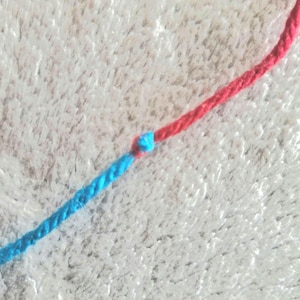 Peut inclure: Deux brins de ficelle, l'un rouge et l'autre bleu, sont noués ensemble.