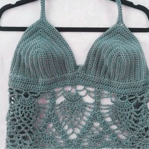 May include: A teal crochet halter top with a delicate lace pattern. The top is made with a soft, lightweight yarn and has a relaxed fit.