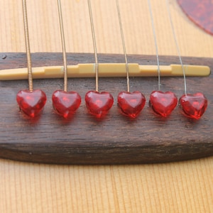 Op de afbeelding: Zes rode hartvormige gitaarstemknoppen op een houten akoestische gitaar.