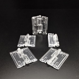 May include: Five clear plastic hinges, each with a central pin and two sets of interlocking plates. The hinges are arranged in a star shape on a black surface.
