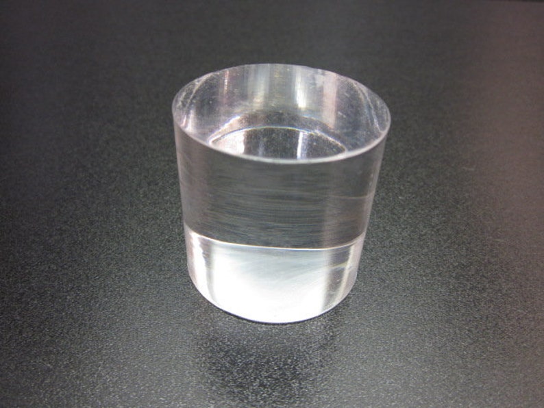 May include: A clear, cylindrical glass with a flat base. The glass is transparent, allowing light to pass through. The object is likely a small tumbler or a decorative piece.