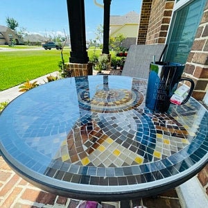 May include: A round, mosaic-tiled table with a blue, brown, and yellow pattern. A black mug with a handle is on the table.