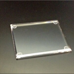 May include: A clear acrylic square display stand with rounded corners and four small clear plastic feet.