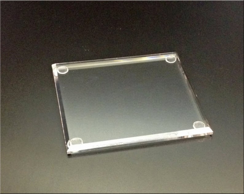 May include: A clear acrylic square display stand with rounded corners and four small clear plastic feet.