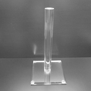 May include: Clear acrylic display stand with a square base and a tall, cylindrical post. The stand is transparent, allowing for a clear view of items placed on it. Ideal for showcasing jewelry, collectibles, or other small items.