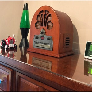 May include: A wooden vintage-style radio with a CD player and a digital clock display. The radio is on a wooden dresser with a glass top. There is a green lava lamp and a red toy tractor on the dresser.
