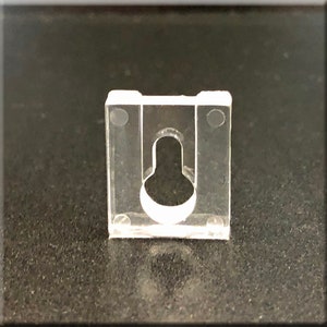 May include: A clear plastic wall mount with a hole in the center. The mount has two small holes on each side.