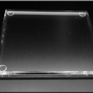 May include: A clear acrylic square coaster with rounded edges and four small, clear rubber feet on the bottom.