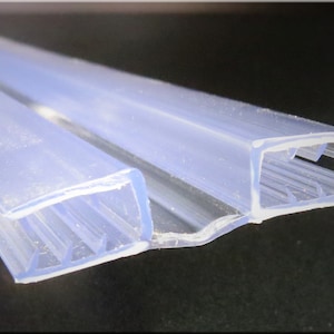 May include: Clear plastic shower door seal with a ribbed design. The seal is designed to fit between two glass panels.