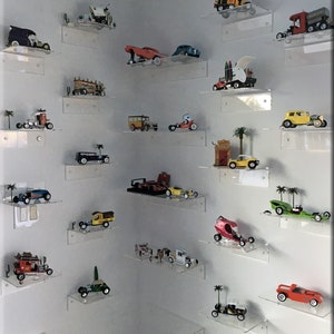 May include: A collection of vintage toy cars displayed on clear acrylic shelves. The cars are in various colors and styles, including a red race car, a yellow school bus, and a green pickup truck.