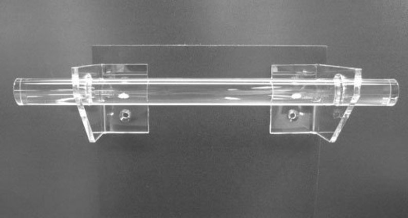 May include: A clear acrylic display rod with two clear mounting brackets. The rod is cylindrical and appears to be hollow. The brackets are rectangular with a right-angle support and screw holes for mounting. The background is a dark gray.