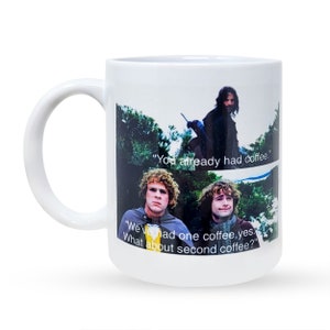 May include: White ceramic mug with a printed image of three characters from the Lord of the Rings movie. The characters are standing in a forest and the text on the mug reads "You already had coffee." "We've had one coffee, yes. What about second coffee?"