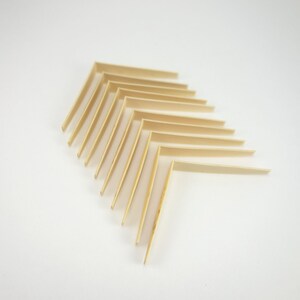 May include: A set of ten wooden corner braces, stacked in a triangular pattern on a white background. The braces are light brown and have a smooth finish.
