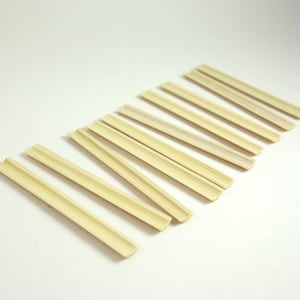 May include: A set of ten natural bamboo straws, arranged in a row on a white background. The straws are all the same size and shape, and they are made of a light brown material.