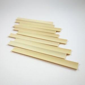 May include: A set of ten natural bamboo skewers, arranged in a staggered pattern on a white background. The skewers are light brown in color and have a smooth, polished finish.