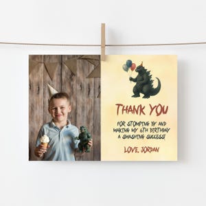 May include: A birthday thank you card with a Godzilla illustration holding balloons. The card reads "Thank You" and "For stomping by and making my 6th birthday a smashing success! Love, Jordan."