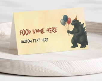 Può includere: Un segnaposto piegato con sfondo giallo chiaro. La carta presenta il testo "FOOD NAME HERE" in rosso e "CUSTOM TEXT HERE" in nero. Un personaggio dei cartoni animati di Godzilla con un cappello da festa tiene in mano dei palloncini.