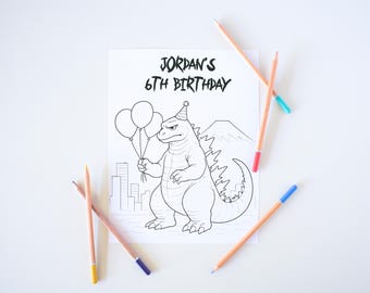 May include: A coloring page with the text "Jordan's 6th Birthday" features a Godzilla-like monster holding balloons, a mountain, and a city skyline. Several colored pencils with different colored tips are scattered around the page.