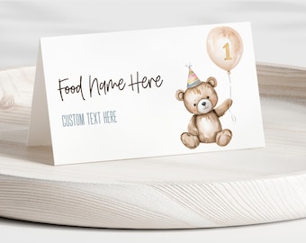 May include: A white folded card with the text "Food Name Here" and "CUSTOM TEXT HERE". A watercolor illustration of a teddy bear wearing a party hat and holding a balloon with the number 1. The card is on a white wooden tray.