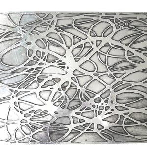 Könnte beinhalten: Eine silberne Metallplatte mit einem erhabenen Design eines netzartigen Musters. Das Muster besteht aus dünnen Linien, die eine Reihe von miteinander verbundenen Formen bilden.