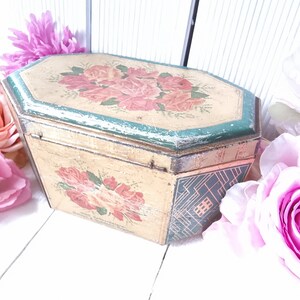 Può includere: Scatola vintage ottagonale in latta con un design floreale con rose rosa e foglie verdi. La scatola è dipinta di color crema con un bordo verde attorno al bordo superiore. La scatola è leggermente usurata e ha un aspetto invecchiato.