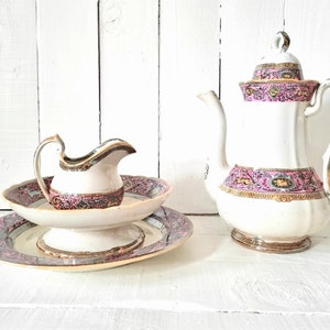 Può includere: Un set da tè vintage con un design floreale rosa e oro. Il set comprende una teiera, un creamer e un piattino abbinato.