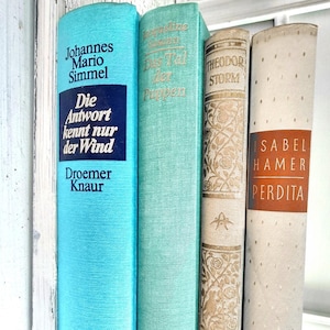 Può includere: Una fila di quattro libri con copertine di colori diversi. Il primo libro è blu turchese con il titolo "Die Antwort kennt nur der Wind" di Johannes Mario Simmel. Il secondo libro è blu turchese con il titolo "Das Tal der Puppen". Il terzo libro è crema con dettagli dorati e il titolo "Theodor Storm". Il quarto libro è crema con dettagli marroni e il titolo "Isabel Hamer Perdita".