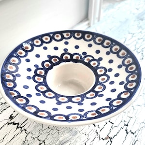 Può includere: Ciotola per salse in ceramica bianca con un pozzetto centrale e un bordo largo. La ciotola è decorata con un motivo a pois blu e marrone. Il bordo presenta un motivo ripetuto di forme a goccia blu e marrone.