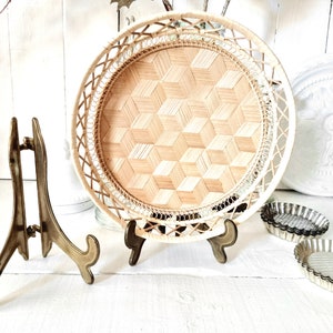 May include: A round woven tray with a geometric pattern sits on a gold metal stand. The tray is made of natural materials and has a light brown color.