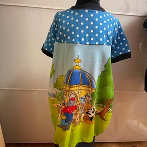 Könnte beinhalten: Ein blaues und grünes Kinderkleid mit einem weißen Tupfenmuster auf der oberen Hälfte. Die untere Hälfte zeigt eine Comic-Illustration von Tieren und einem Gebäude mit einer blauen Kuppel.