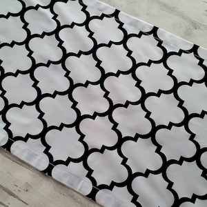 Könnte beinhalten: Ein geometrischer Tischläufer in Schwarz und Weiß mit einem sich wiederholenden Muster aus Vierblättern. Der Läufer ist aus Stoff und hat einen weißen Hintergrund mit schwarzen Vierblättern.