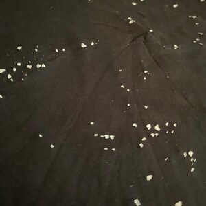 May include: Black fabric with a pattern of small, irregular white shapes. The shapes are scattered across the surface, creating a speckled effect. The fabric appears to be a dark color, possibly a shirt or other clothing item.