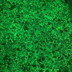 May include: Close-up of a textured surface with a repeating pattern of irregular, leaf-like shapes. The shapes are a vibrant, glowing green, creating a sense of depth and organic texture. The overall effect is abstract and visually striking.