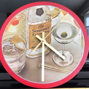 May include: A red and white round clock with a gold-colored face. The clock face features a bottle of Seagram's Extra Dry Gin, a martini glass, and a glass of ice. The text "The Perfect Martini Gin" is printed on the bottle.