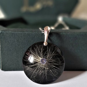 May include: A silver pendant necklace with a round black resin charm containing a small amount of hair and a purple gemstone in the center.
