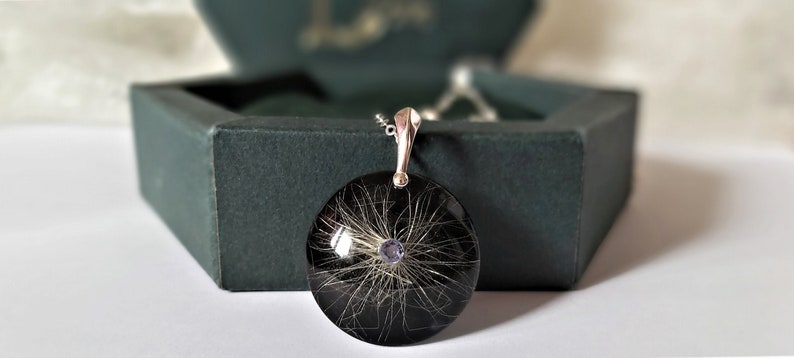 May include: A silver pendant necklace with a round black resin charm containing a small amount of hair and a purple gemstone in the center.