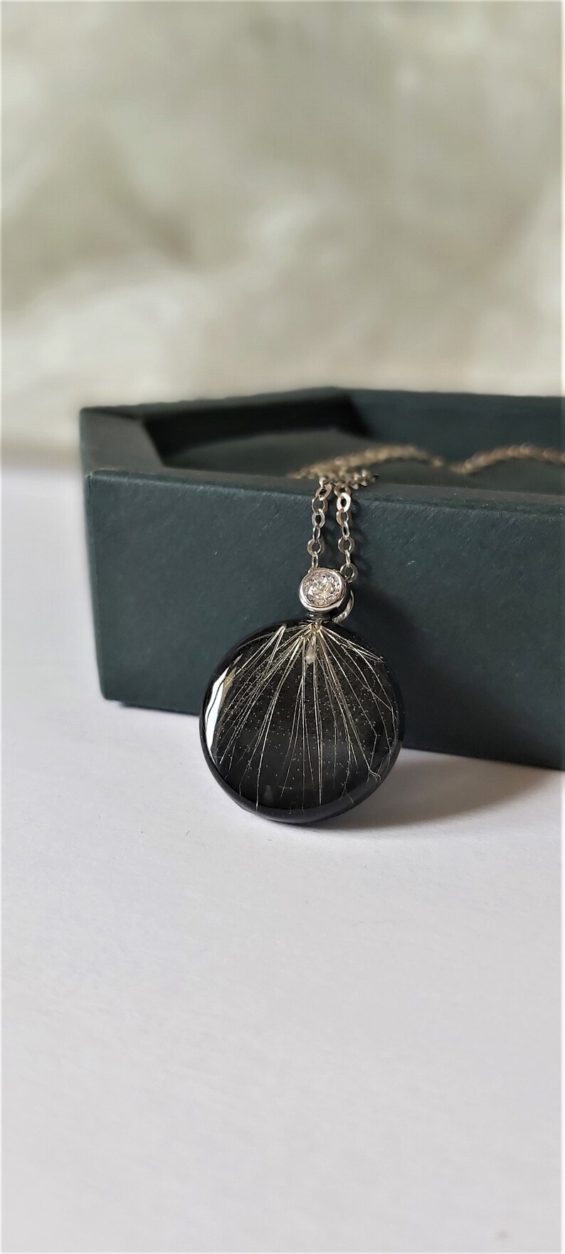 Puede incluir: Un collar de cadena de plata con un colgante redondo negro que presenta un delicado dise&ntilde;o de diente de le&oacute;n blanco y un peque&ntilde;o acento de cristal transparente.
