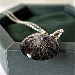 May include: A silver necklace with a black round pendant containing a small amount of hair and a purple gemstone in the center.